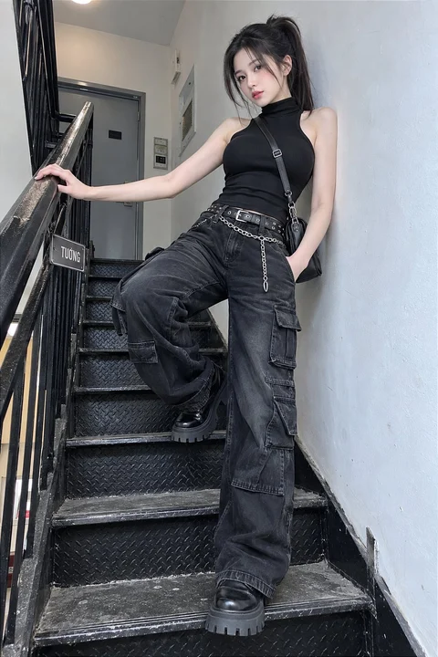 A person in a black sleeveless top and dark cargo trousers stands on a metal staircase.